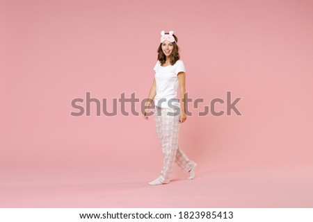 Full length side view portrait of smiling young brunette woman in white pajamas home wear sleep mask looking camera rest at home isolated on pink background studio. Relax good mood lifestyle concept Royalty-Free Stock Photo #1823985413