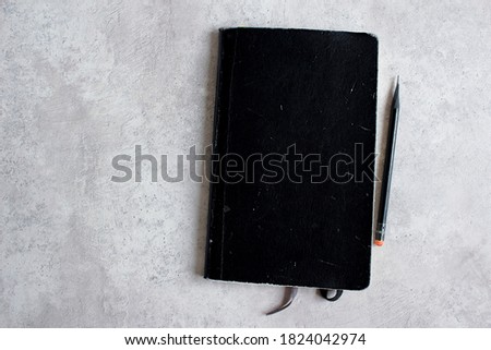 Black notebook on a cement background. Notepad with blank cover for text, illustration. Notepad and pencil.