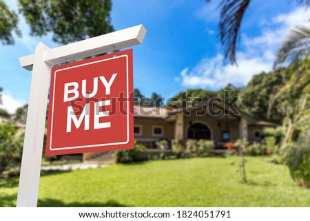 A yard sign with the words Buy Me in front of a bungalow style house. Real estate concept.