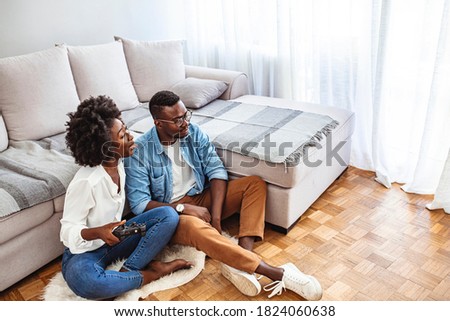 Happy couple on the couch playing video games at home in the living room. Close up of smiling couple lying on the floor playing video games. Young Couple In Pajamas Playing Video Game Together