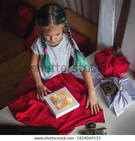 Zero waste Christmas wrapping. Cute girl learning to wrap gifts in traditional Japanese style furoshiki via internet, online educational video. Sustainable celebration