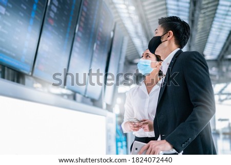Smart asian businessman and businesswoman wear mask protection in airport terminal,discuss and planning business strategy while waiting flight on information board background.Partner meeting concept. Royalty-Free Stock Photo #1824072440