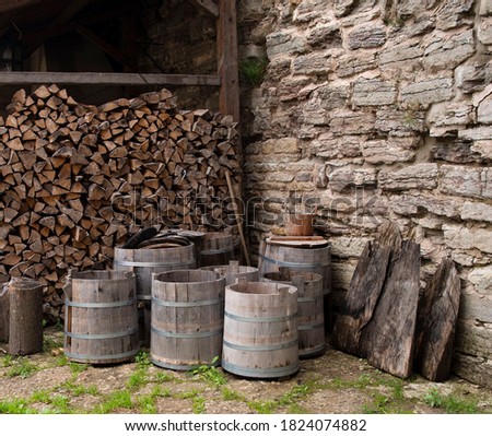 There are barrels and tubs near the wall of the medieval castle, in the background there is a woodpile of chopped wood for the stove. Royalty-Free Stock Photo #1824074882