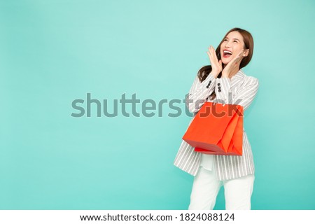 Portrait of excited screaming young asian woman holding shopping bag isolated over green background, Wow and surprised concept