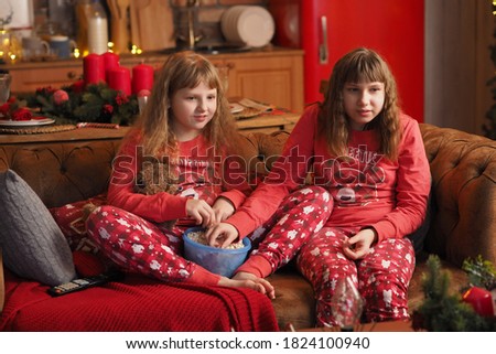 two teenage girls with loose hair in red pajamas are watching a movie, laughing and eating popcorn.