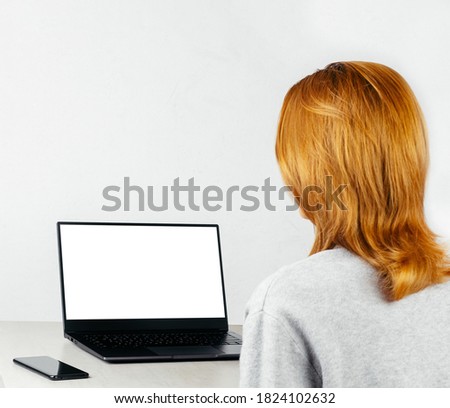 red-haired girl sitting with smartphone and laptop with white mock-up, concept online training, communication, remote work
