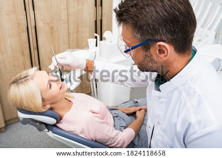 Handsome dentist examines a beautiful mature female patient with special dental tools in a modern dental clinic. Stomatology and health care concept