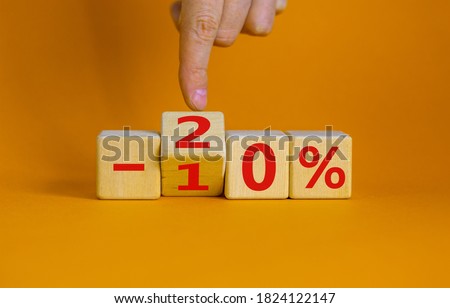 Hand turns a cube and changes the expression '-10 percent' to '-20 percent'. Beautiful orange background, copy space. Business concept.
