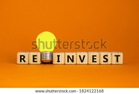 Wooden cubes with word 'reinvest'. Yellow light bulb. Beautiful orange background. Business concept. Copy space.