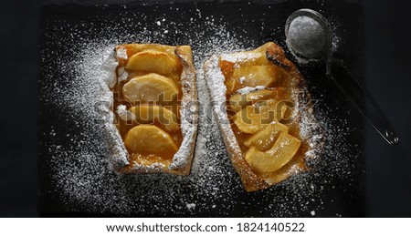 Apple phyllo tart sprinkled with icing sugar on dark background.