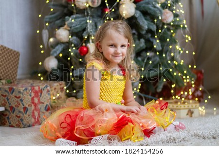 Portrait of a little cute girl in an elegant carnival dress against the background of Christmas tree lights, New Year's photo session for a child, winter holidays.
