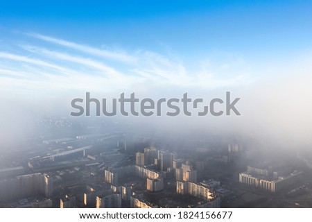 The city is under a layer of fog and low clouds, from above there is a clear blue sky