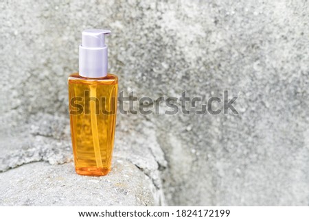 An orange oil bottle next to natural stones against a gray wall with natural light. Trendy style. Cosmetic mockup. Copyspace.
