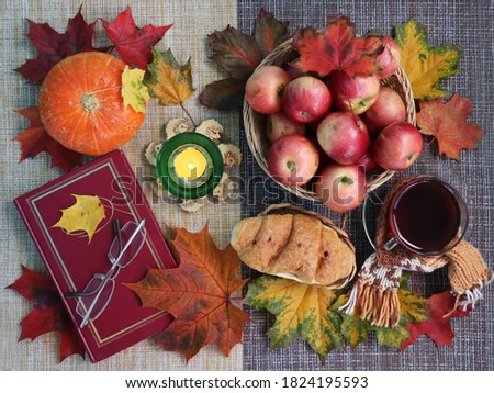 Cup of tea and croissant in autumn leaves background. Book with glasses,apples and pumpkin on the table. Fall decoration. Top view background.