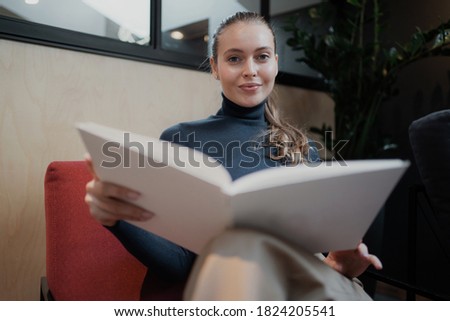 An interesting edition of the new story. Sits in a comfortable chair. confident beautiful blonde woman of European appearance reads a romantic fairy tale open book.