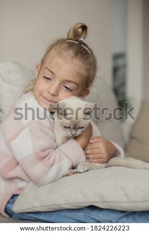 little girl hugging kitten on sofa.