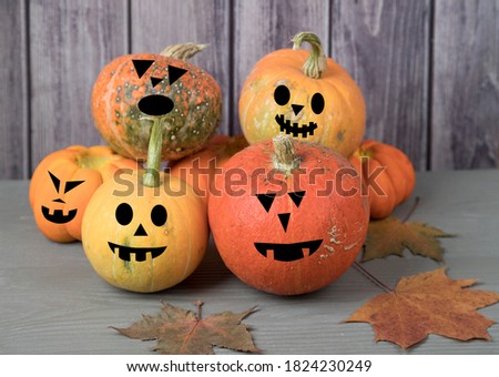 Pyramid of pumpkin harvest with awesome masks with autumn leaves on a gray wooden background before the Halloween holiday.