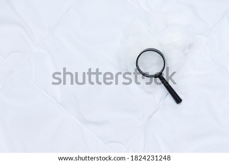A black magnifier lies on white blanket. Detecting bed bugs in bedroom.