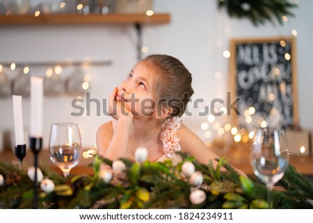 Little girl is bored sitting at the festive table on Christmas night.