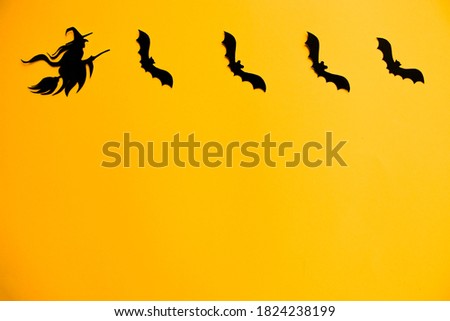Silhouettes of black bats and witch on broom made of paper on orange background. Halloween greeting template with copy space. Flat lay for your design.
