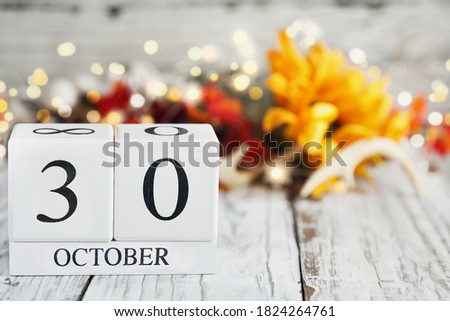 White wood calendar blocks with the date October 30th and autumn decorations over a wooden table. Selective focus with blurred background. 