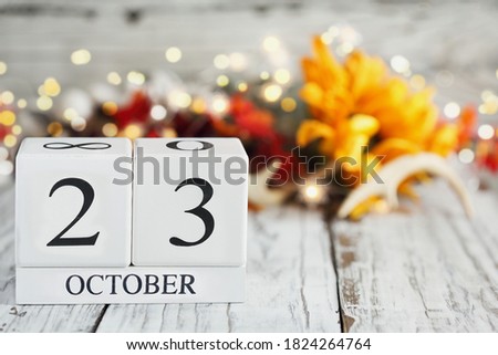 White wood calendar blocks with the date October 23rd and autumn decorations over a wooden table. Selective focus with blurred background. 