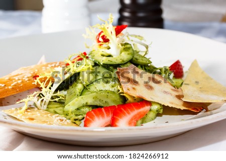 Salad with avocado, strawberries, frieze salad and chips is on the plate