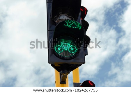Closeup to a green traffic light near to a vehicular traffic light in a bike path crossroad with blue cloudy sky at background. 