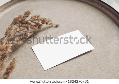Closeup of blank business card mockup. Dry grass on beige ceramics plate. Fall and Thanksgiving concept. Autumn styled stock still life photo. Selective focus, no people.