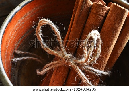 A close up image of several brown cinnamon sticks in a reddish brown handmade pottery bowl. 