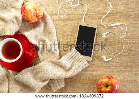 Phone mockup, sweater, cup of tea and apples on the wooden background. Cozy autumn or winter consept.