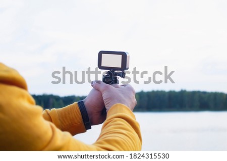 Tourist shoots a video on an action camera against the backdrop of nature and the river. Close-up of a white screen mockup on the camera