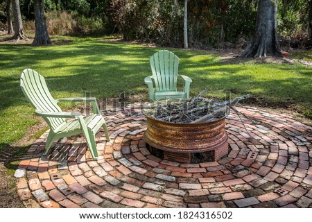 An outdoor fire pit with Adirondack chair seating on an outdoor brick patio near a pond at a cabin rental in Georgia