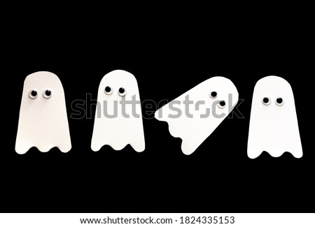 white paper ghost on black background with plastic eyes. Halloween. paper crafts. Seasonal fun.