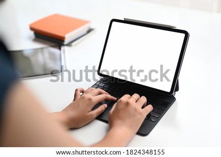 Businesswoman working on her project while typing on tablet computer with white screen in modern office.