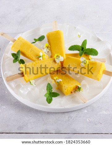 Healthy homemade mango and yogurt popsicle, garnish with edible flowers and mint leaf, for summer ice cream dessert concept.