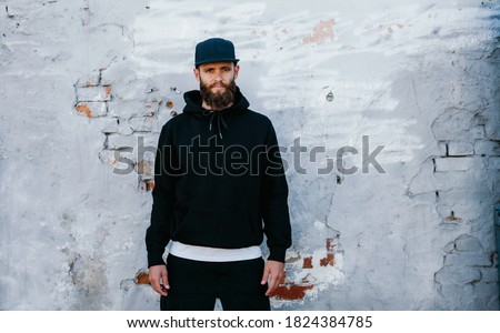 City portrait of handsome guy wearing black blank hoodie and baseball cap with space for your logo or design. Mockup for print