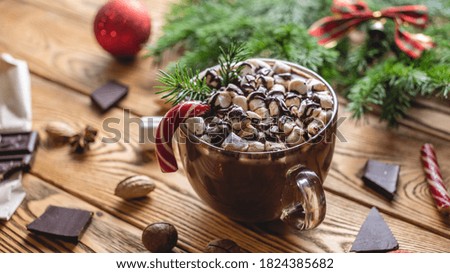 A cup of aromatic tasty hot chocolate with marshmallows decorated with red candy on a wooden table surrounded by Christmas accessories. Concept of a festive atmosphere and cozy New Year mood.