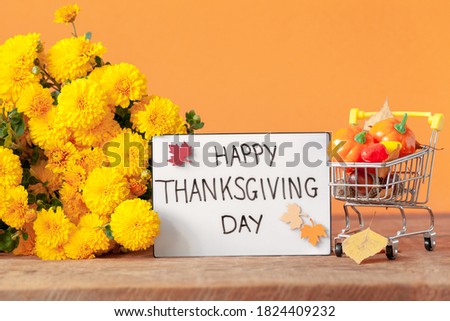 Thanksgiving autumn composition with yellow flower and shopping cart with pumpkins and acorns on orange background. Lightbox with the phrase Happy thanksgiving day. Autumn holidays, fall concept.