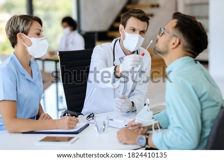 Doctor wearing protective face mask and using cotton swab while doing PCR test of a patient during coronavirus pandemic.  Royalty-Free Stock Photo #1824410135