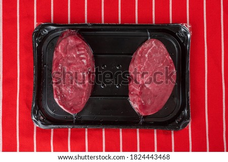 Two fresh fillet steaks on a plastic tray on a red and white butcher apron. Meat and retail industry concept. Premium cut of beef. Royalty-Free Stock Photo #1824443468