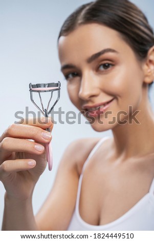 Close up portrait of happy cheerful woman holding eyelashes tool in hand in front of her while posing at the photo camera
