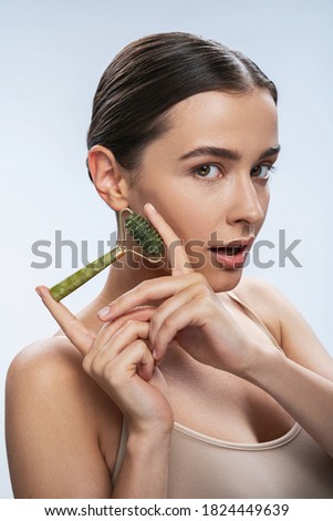 Studio portrait of young pretty lady with roller green quartz in arms isolated on white background