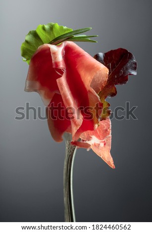 Prosciutto with rosemary and salad leaves on a dark background.