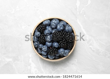 Blueberries and blackberries on light marble table, top view