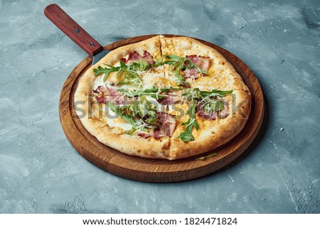 Pizza with bacon, white sauce and yolk on a wooden board on a gray background. Classic Italian cuisine