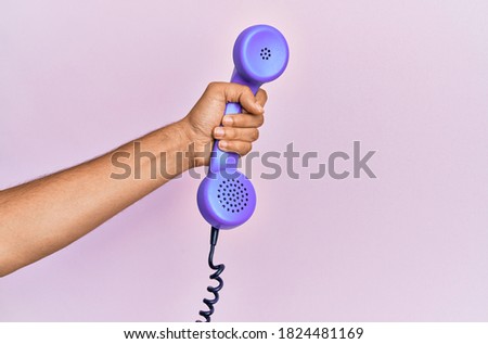 Hispanic hand holding vintage telephone over isolated pink background.