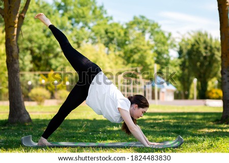 Yoga. A young woman in sportswear performing the dog face-down exercise is engaged in a Park on the grass. The concept of sport for a healthy lifestyle