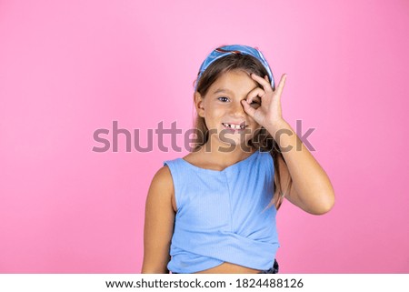 Young beautiful child girl over isolated pink background doing ok gesture shocked with smiling face, eye looking through fingers