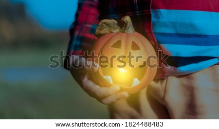 Kid's hand holding Jack'O pumpkin lamp, trick or treat on Halloween day. Concept for autumn holidays background.